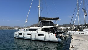 Un puerto deportivo con varios veleros amarrados, cielo despejado y un paisaje montañoso al fondo.