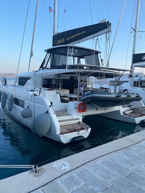 A white yacht docked at a marina with a website banner, life rings, and a clear sky.