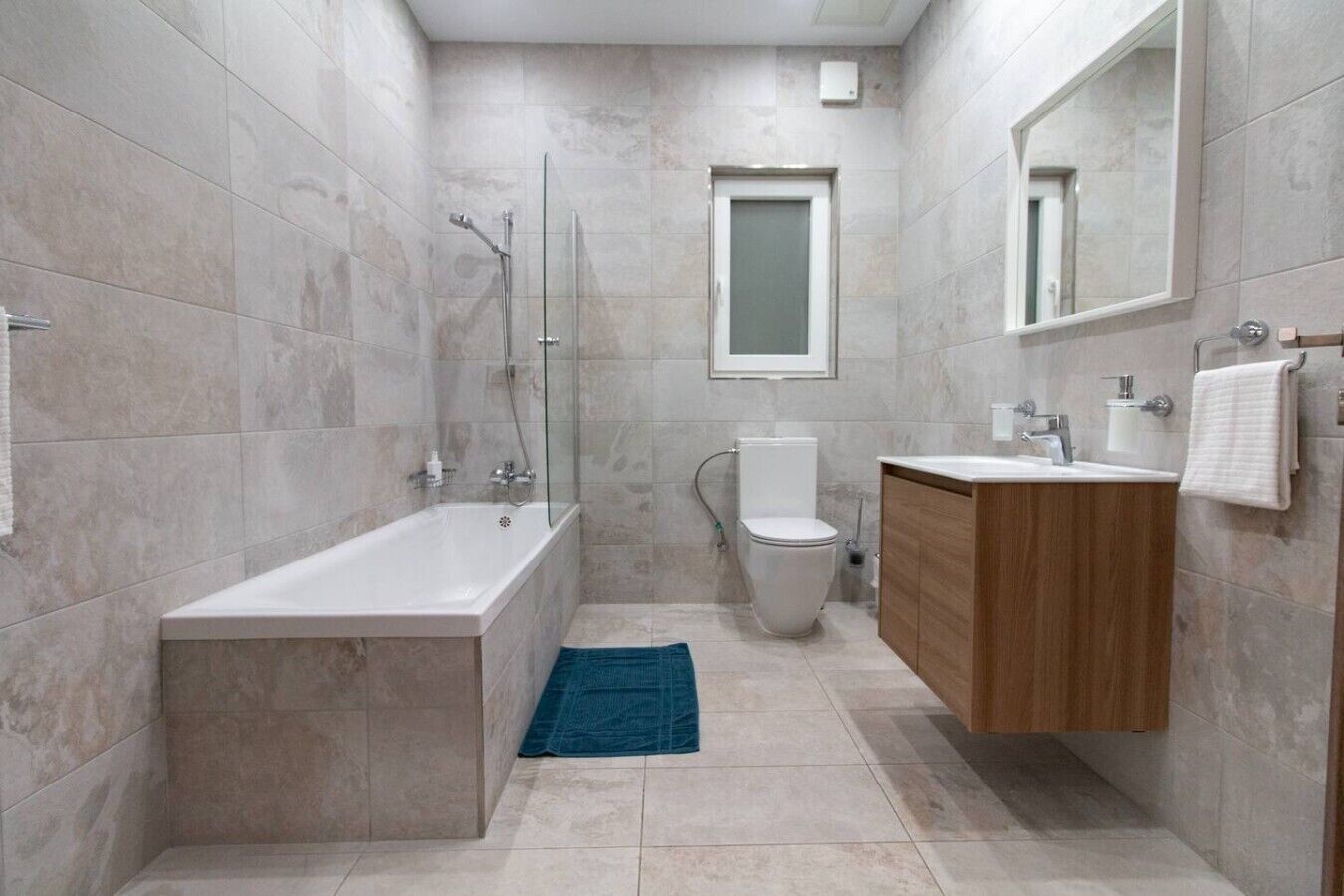 A modern bathroom with a bathtub, toilet, and wooden vanity.