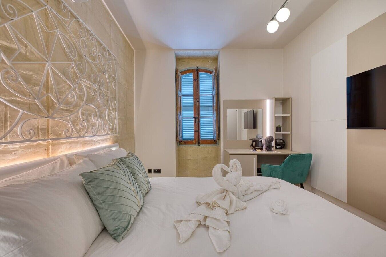 A hotel room with a bed, a desk, a chair, a TV, and a window with shutters.