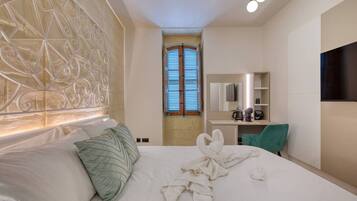A hotel room with a bed, a desk, a chair, a TV, and a window with shutters.