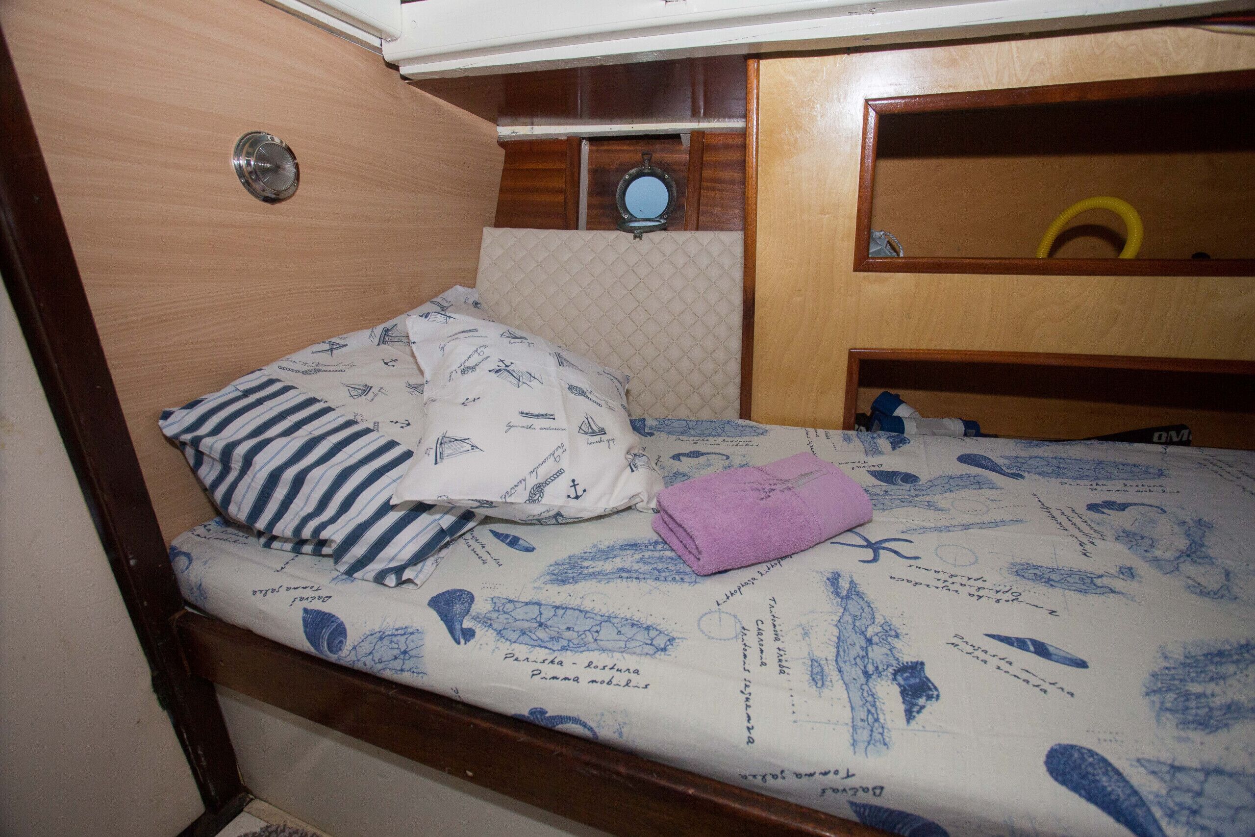 Een klein, compact bed met een gewatteerd hoofdbord, een houten plank met een spiegel en een klein kastje.