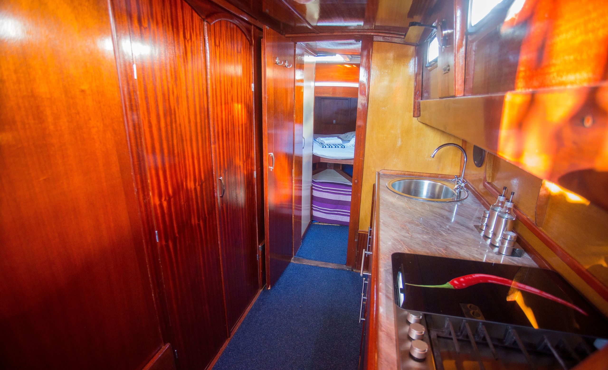 A narrow corridor leading to a small cabin with a bed, a sink, and a stove.