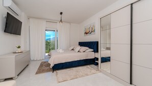 Ein Schlafzimmer mit Bett, Fernseher, Kleiderschrank und Blick auf Grünflächen.