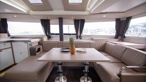 A modern interior with a dining area, cushioned seating, and a view through large windows. - Sun-Kissed Sailing Adventure in Islas Cícladas, Mykonos (Mykonos)