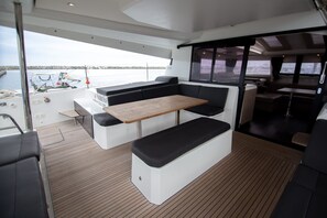 A boat interior with a wooden table, black cushioned seating, and a view of the water.