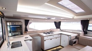 A compact kitchen with a stove, sink, and storage cabinets, a dining area with a table and chairs, and a window providing a view. - Sun-Kissed Sailing Adventure in Islas Cícladas, Mykonos (Mykonos)