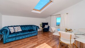 Una sala de estar con un sofá azul, una mesita con una planta, un sillón azul y una mesa de comedor de vidrio con sillas.