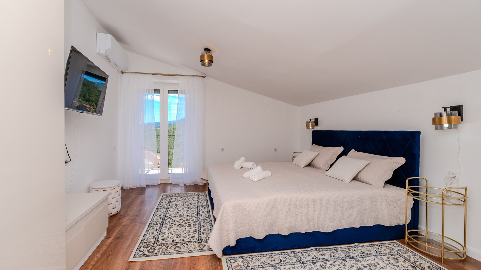 Een slaapkamer met een bed, een televisie, een raam met gordijnen, een wandairconditioner en een nachtkastje.