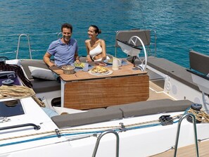 A boat with a dining area, a table with plates and a pitcher, and a person seated at the table. - Sun-Kissed Sailing Adventure in Islas Baleares, Mallorca (Palma)