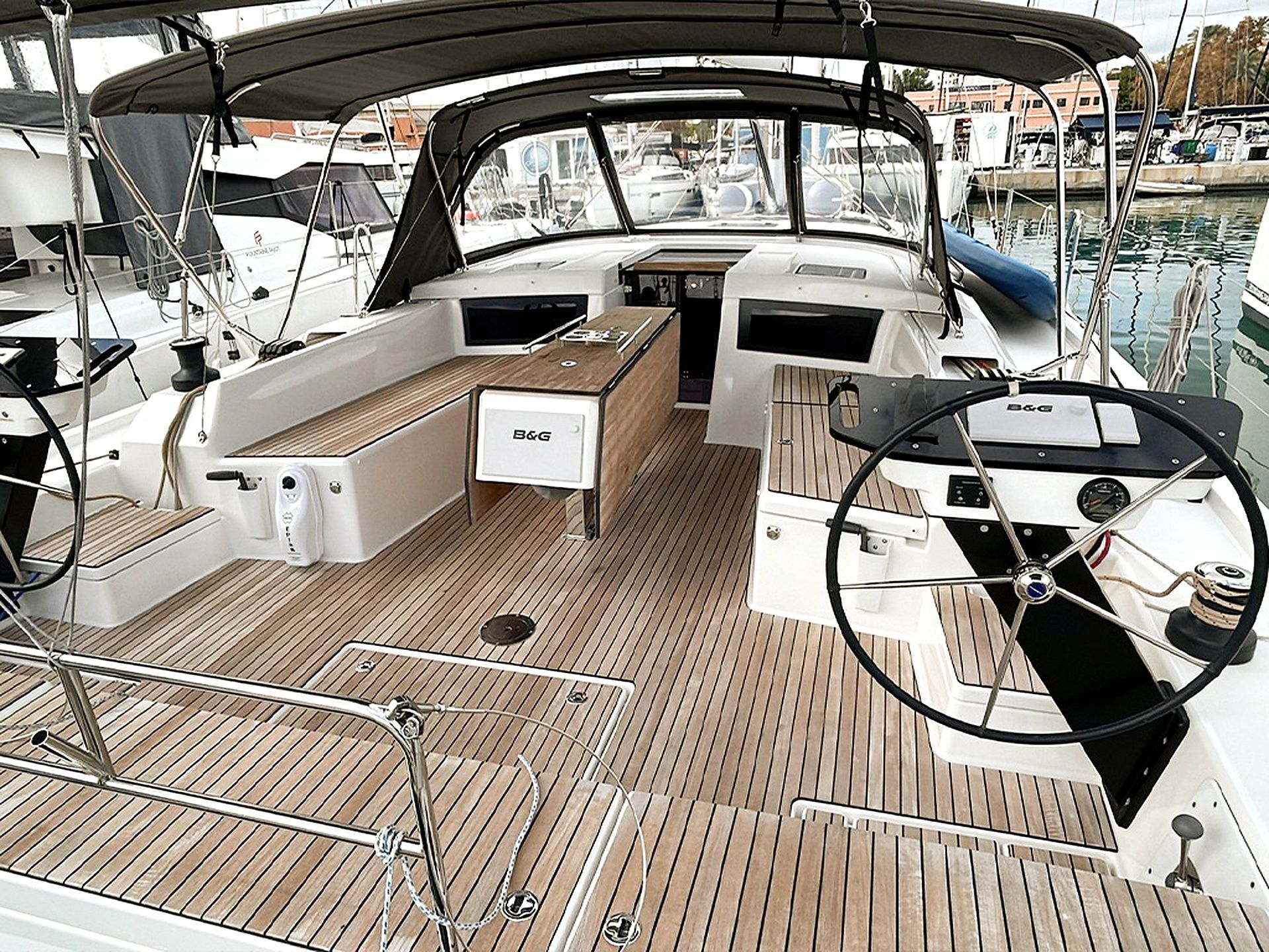 A boat's deck with a steering wheel, a B&G brand control panel, and a wooden floor.