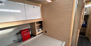 A compact kitchen area with a white cabinet, a red appliance, and a wooden shelf.