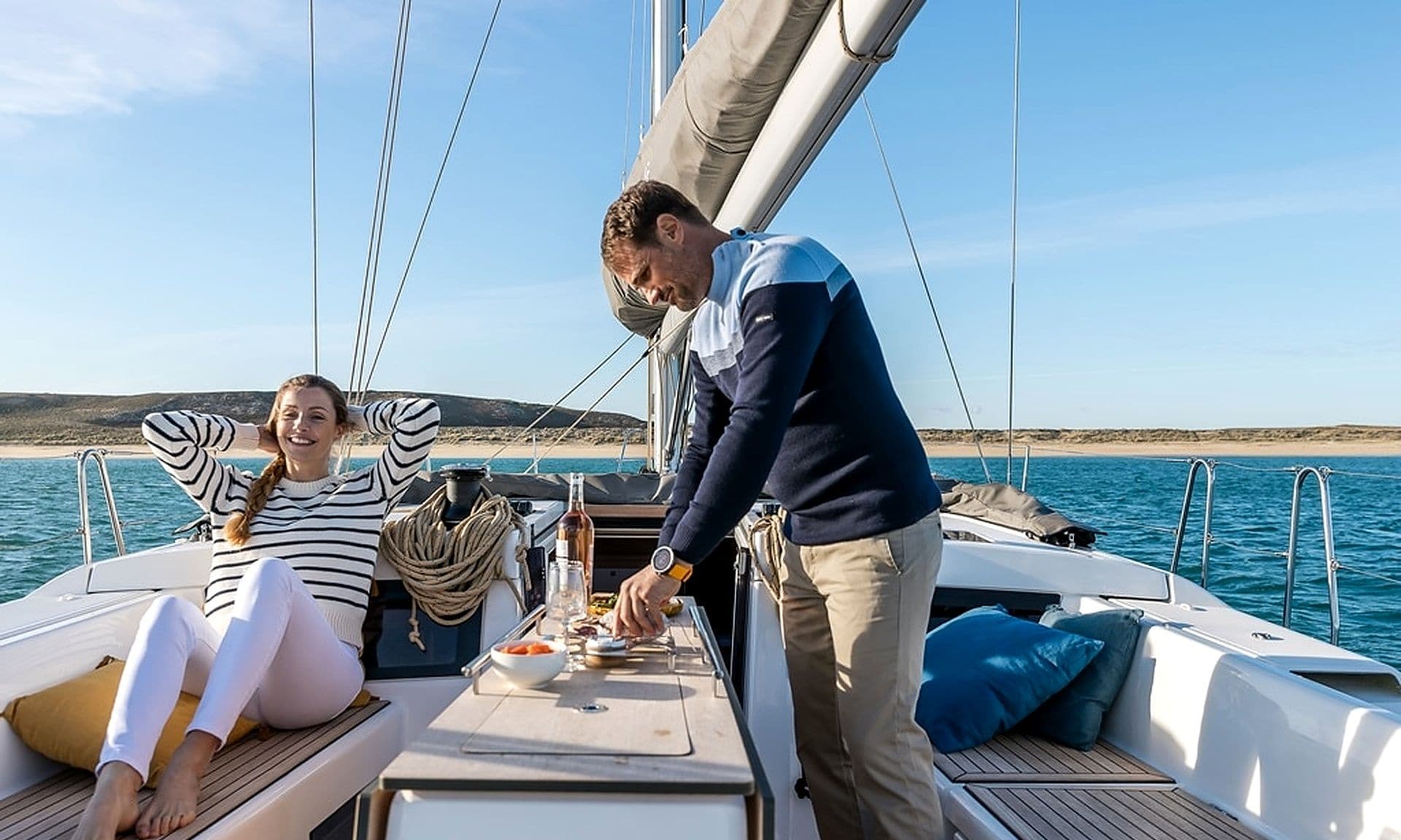 A sailboat with a dining table, two people seated, and a person standing.