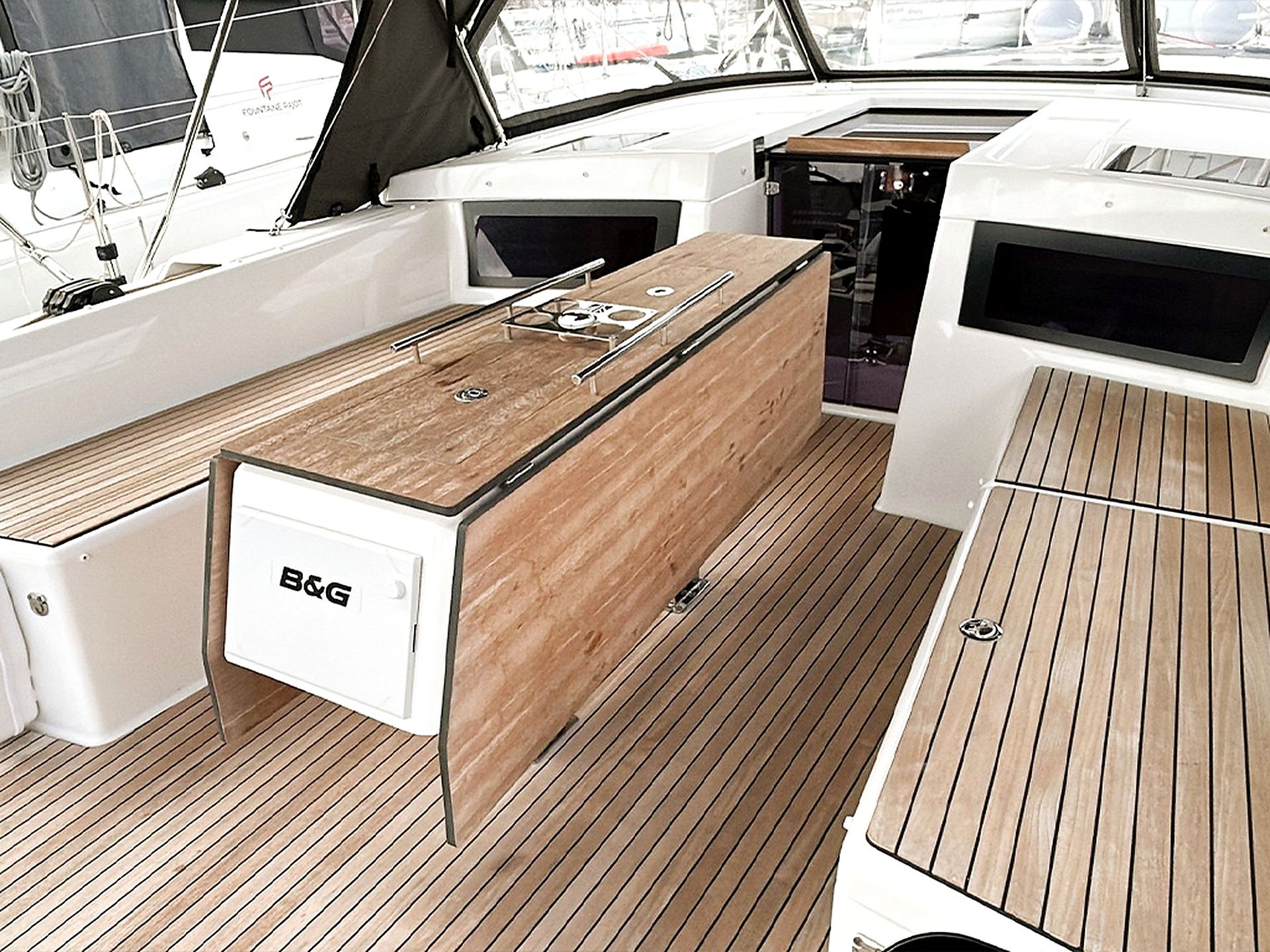 A boat's deck with a central wooden table, a B&G refrigerator, and a white cabinet.