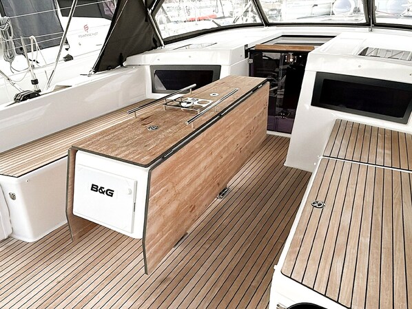 A boat's deck with a central wooden table, a B&G refrigerator, and a white cabinet.