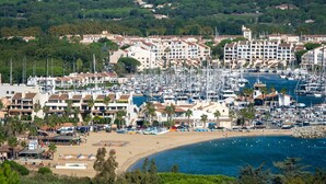 Un port de plaisance situé sur la côte, avec de nombreux bateaux, une plage de sable et des immeubles résidentiels dotés de balcons.