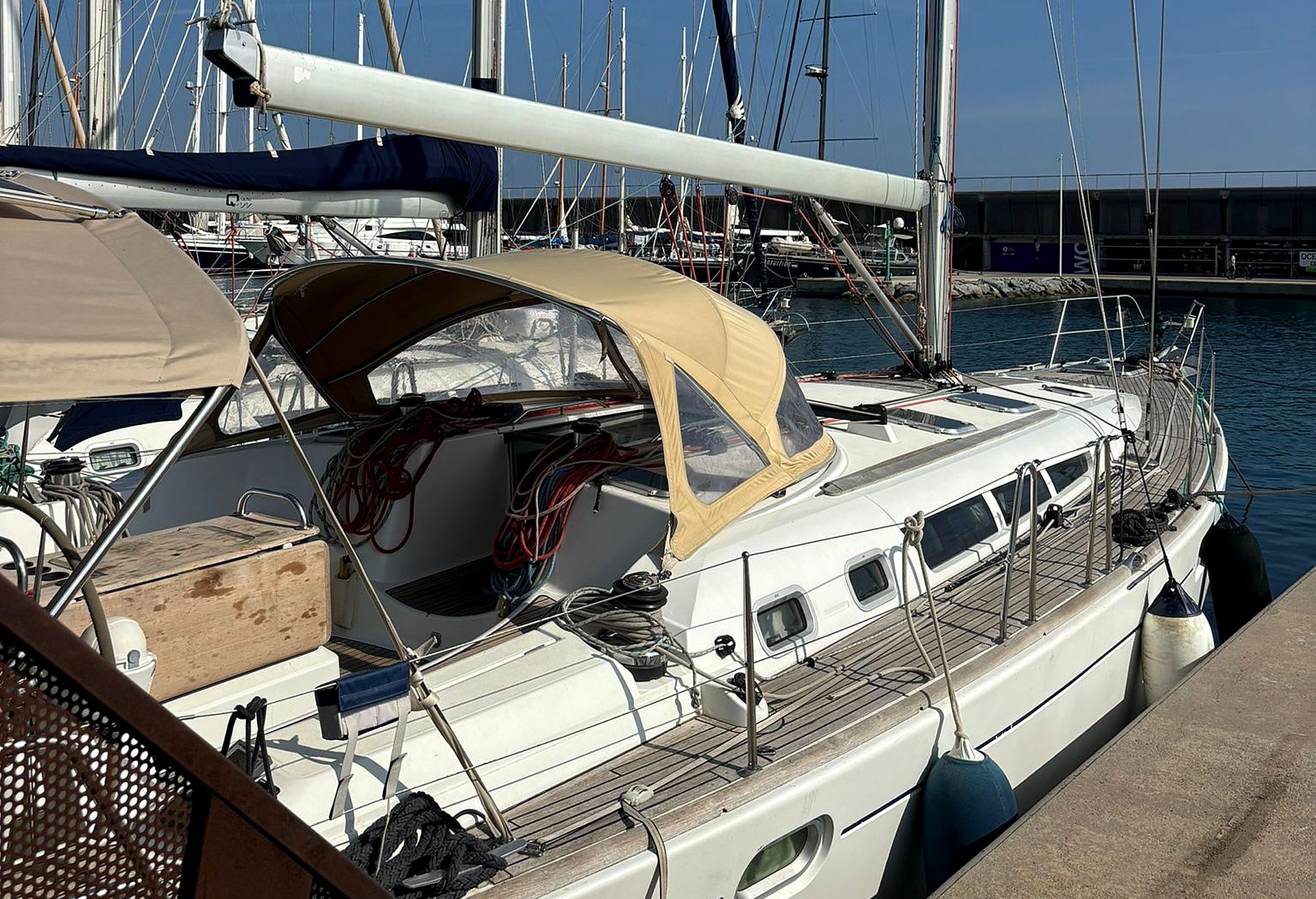 Un velero amarrado en un puerto deportivo, con cubierta protegida, múltiples escotillas y una red de cuerdas.