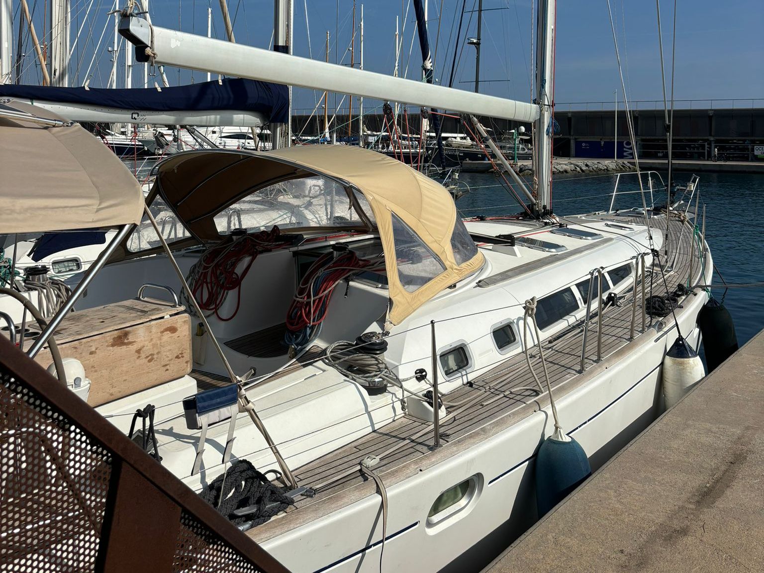 Un velero amarrado en un puerto deportivo con una cubierta techada, camarote con ventanas y una pequeña zona de cubierta.