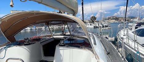 A sailboat's deck with a steering wheel, ropes, and a view of the marina.