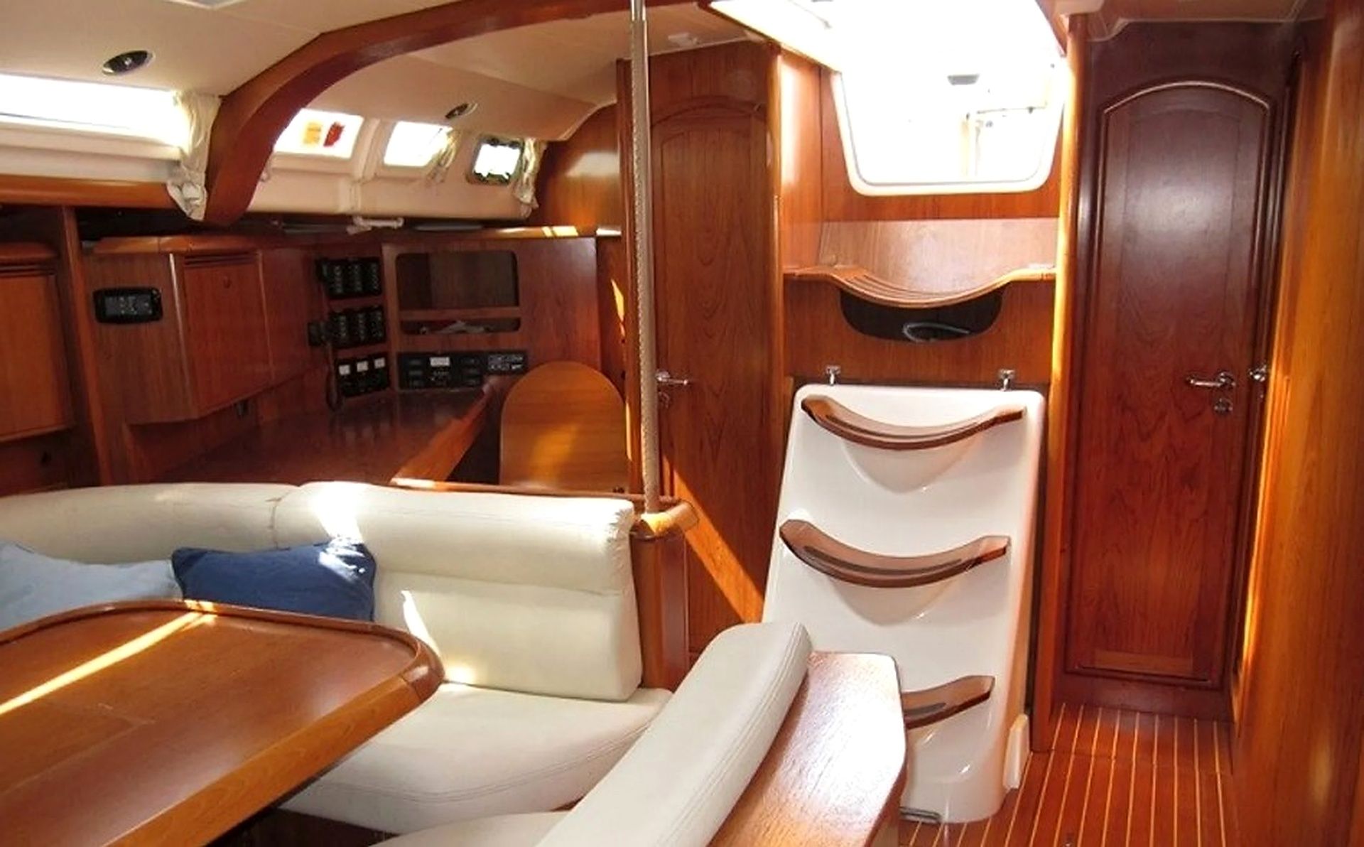 Interior de un barco con zona de estar, una mesita, un baño y una puerta.