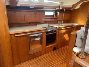 A compact galley with wooden cabinetry, a stove, and a sink. - Sun-Kissed Sailing Adventure in Provence-Alpes-Côte d'Azur (Grimaud)