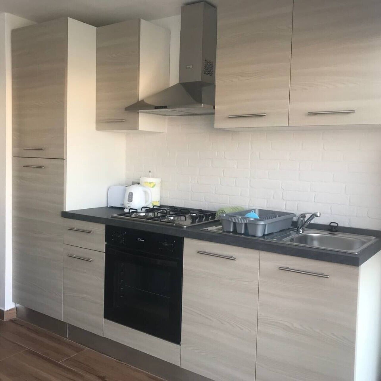 A modern kitchen with light wood cabinets, a black dishwasher, a gas stove, and a stainless steel sink.