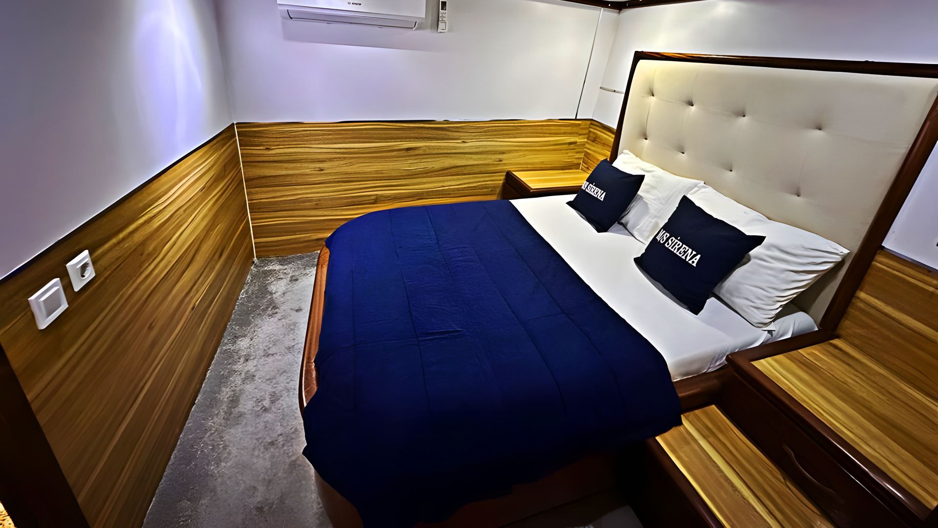 A bedroom with a wooden headboard, a bed with blue bedding, and two pillows with text.
