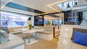 A modern yacht interior with a dining area, seating, and a view of the marina.