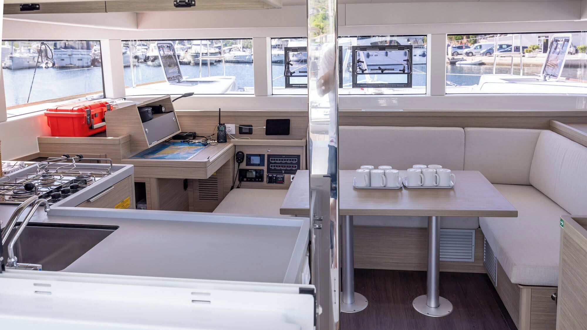 L'intérieur d'un bateau comprend un espace cuisine, un panneau de commande, un coin salon avec une table et des chaises, ainsi que des fenêtres donnant sur le port de plaisance.