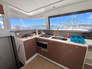 A compact galley kitchen with a stove, sink, and storage cabinets, overlooking a marina with boats.