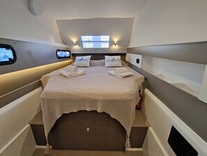 A compact, well-lit cabin with a bed, two pillows, a small window, and a mounted screen.