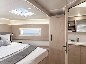 Une chambre avec un puits de lumière, un lit avec des oreillers, une table de chevet et une armoire en bois.