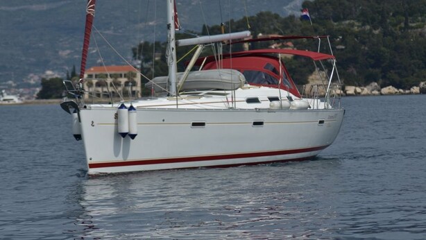 Een witte zeilboot met een rode streep, een kajuit en een mast, drijvend op kalm water met een bergachtige achtergrond.