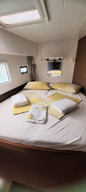 A bed with pillows and towels, a small window, and a mirror.