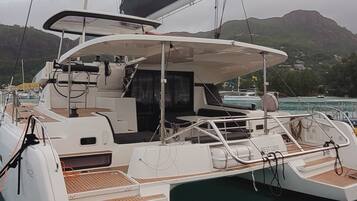 A white yacht docked at a marina with a covered deck area and a view of a mountainous landscape in the background.