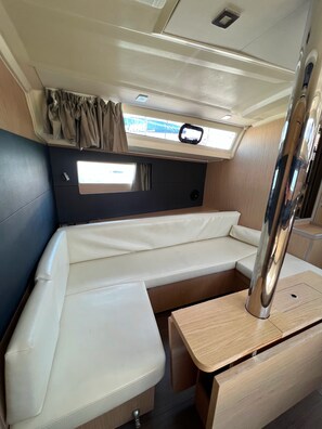 A compact RV interior with a cushioned bench seating area, a small table, and a window with curtains. - Sun-Kissed Sailing Adventure in the Ionian Islands, Lefkada (Lefkada)