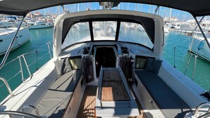 A boat deck with a steering wheel, a cushioned seating area, and a view of the marina. - Sun-Kissed Sailing Adventure in the Ionian Islands, Lefkada (Lefkada)
