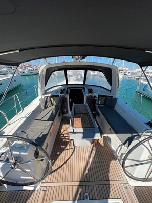 A boat deck with a steering wheel, a cushioned seating area, and a view of the marina. - Sun-Kissed Sailing Adventure in the Ionian Islands, Lefkada (Lefkada)