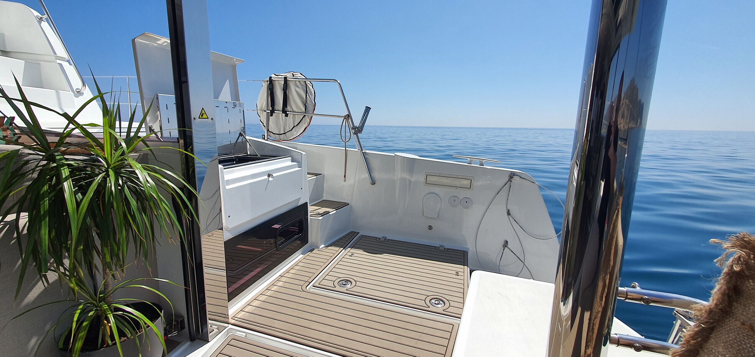 A boat deck with a small seating area, a potted plant, and a view of the water.