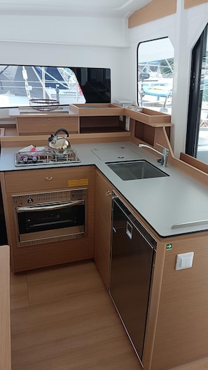 Eine kleine Küche mit Spüle, Herd und Backofen, ausgestattet mit Holzschränken und einem Fenster mit Blick auf Boote.