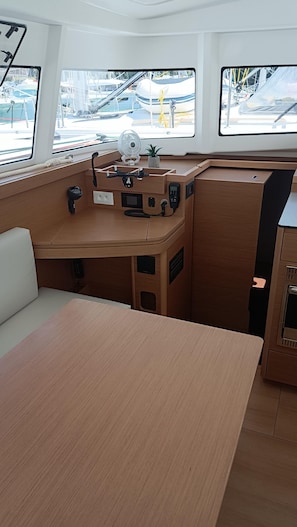 Das Interieur eines Bootes mit einem Holztisch, einer gepolsterten Bank, einer Armaturentafel und Blick auf den Hafen durch die Fenster.