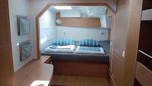 A compact RV interior with a bunk bed, a small seating area, and a window.