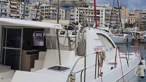 Uno yacht bianco ormeggiato in una marina con un tendalino blu e un pannello di controllo sul ponte.