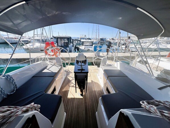 Een bootdek met zitplaatsen, een stuurwiel en een uitzicht op andere boten in een jachthaven.