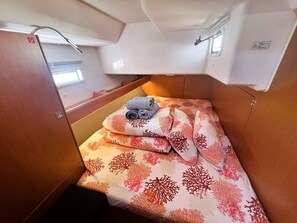 Een compacte hut met een enkel bed, een bedspread met dessin, een klein tafeltje met een opgerolde handdoek, en een raam dat natuurlijk licht binnenlaat.