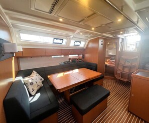 Ein kompakter Innenraum mit einer Couch, einem Tisch und einer Bank. Deckenleuchten und ein Fenster sind vorhanden.