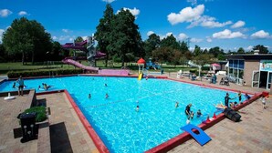 A swimming pool with a water slide and a play structure in the background. - Nature Base Near Fishing Waters (Heinkenszand)