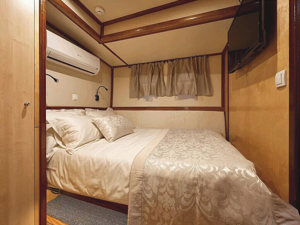 Een slaapkamer met een bed, een raam met gordijnen, een airconditioning en een aan de muur bevestigde televisie.