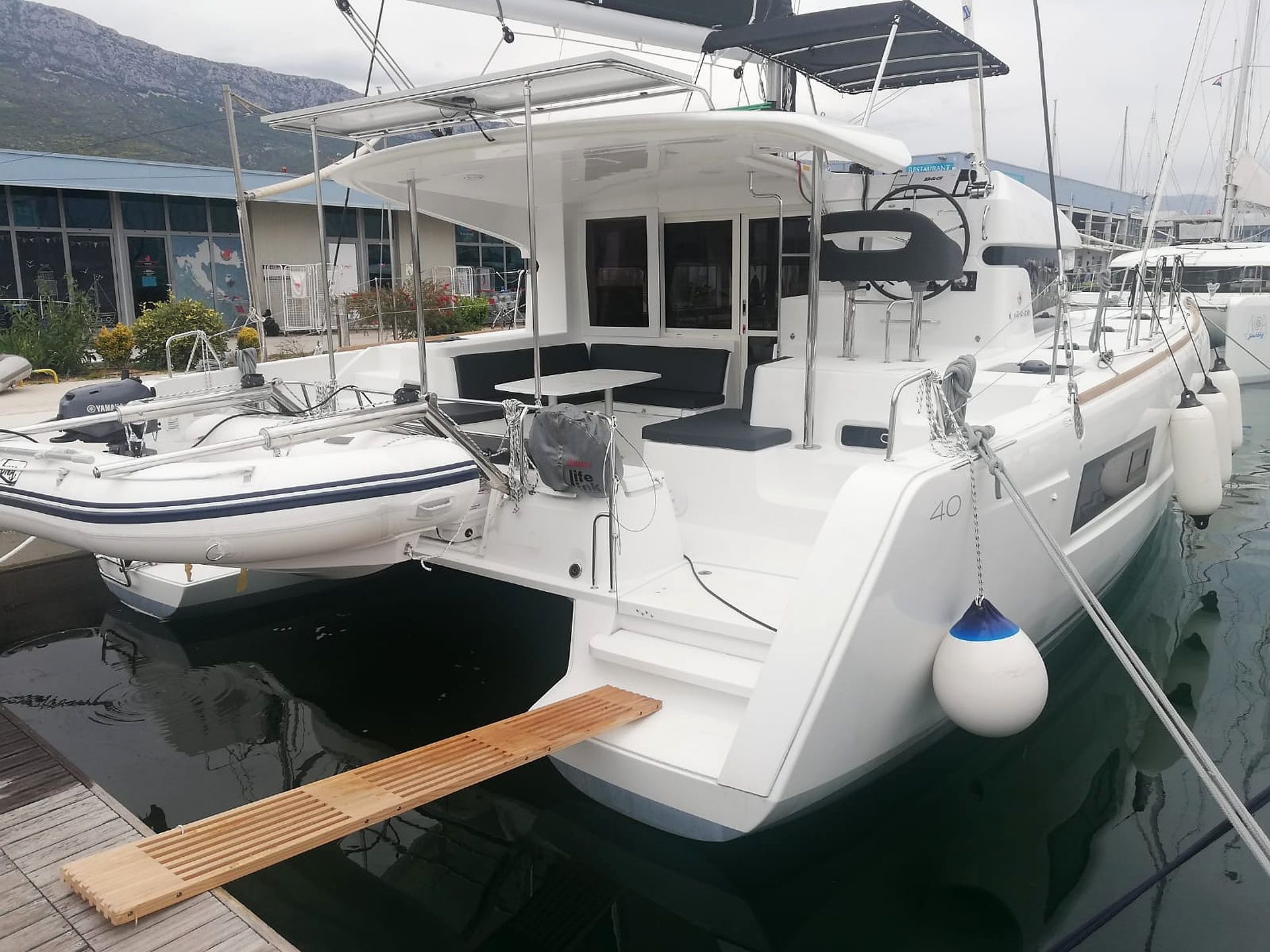 A white yacht docked at a marina with a wooden deck, a small table, and a seating area.