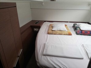 A neatly made bed with a white comforter, a folded blanket, and a colorful throw. There is a wooden nightstand with a lamp and a power outlet.